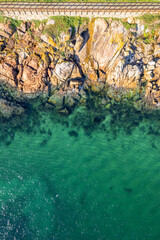 zenithal aerial drone view of a rocky coastline with a wooden pedestrian walkway, background for summer concept