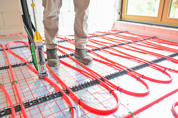 A technician skillfully installs an underfloor heating system using advanced technology, showcasing precise placement and modern plumbing techniques in a construction setting