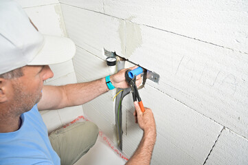 A technician is using a pressure gauge and pliers to inspect plumbing work on a wall, showcasing practical home maintenance skills and service tools being used