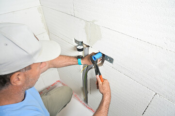 A technician is using a pressure gauge and pliers to inspect plumbing work on a wall, showcasing...