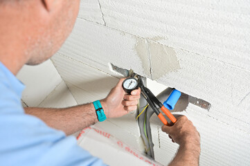 A technician is using a pressure gauge and pliers to inspect plumbing work on a wall, showcasing practical home maintenance skills and service tools being used