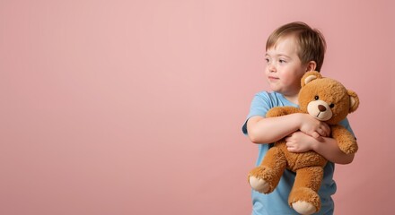Child with Down syndrome hugging teddy bear against pink background. Caucasian boy in blue t-shirt holding brown plush toy. Comfort object concept. World Down Syndrome Day. Childhood innocence