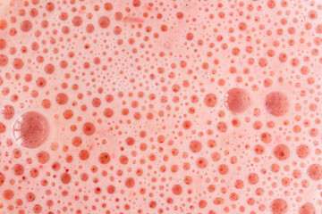 Pink foam texture with small bubbles on a light pink background. Close up macro view of liquid...