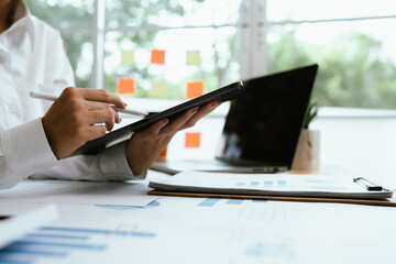 Naklejka premium Close up of professional businessman sitting at desk in modern office, analyzing charts and financial documents, planning business growth and investment strategy.