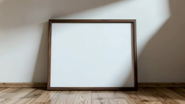 A large empty wooden picture frame rests against a white wall on a wooden floor in a minimalist room.