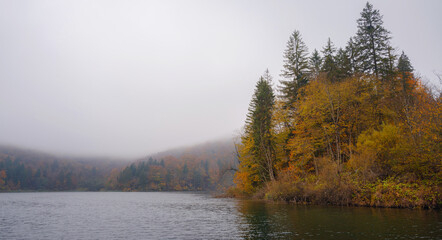 Fototapeta premium Plitvice Lakes in Croatia during autumn, showcasing stunning waterfalls, vibrant foliage, and crystal-clear waters, creating a magical and serene natural landscape. Lake fog with Autumn foliage