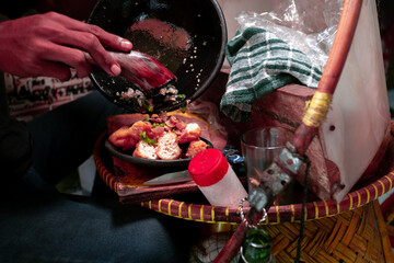 The preparation of Tahu Gejrot, a traditional dish from Cirebon, West Java, is shown. Hands are pouring a dark, spicy sauce with shallots and chilies over fried tofu on a plate.