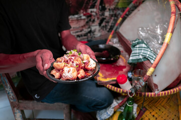  a plate of Tahu Gejrot, a Cirebon dish, being held by a vendor. The fried tofu is topped with a dark, spicy sauce, shallots, and chilies.