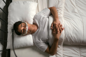 Man sleeping on back with CPAP mask to treat snoring and obstructive sleep apnea (OSA). Promotes respiratory therapy, sleep health, and nighttime breathing support in home environment.