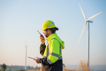 Engineer wearing uniform inspection and survey work in wind turbine farms rotation to generate electricity energy. Maintenance engineer working in wind turbine farm at sunset.