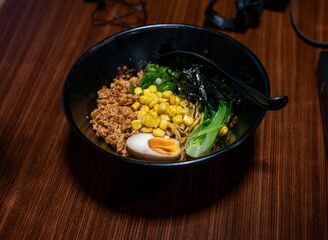 A vibrant bowl of dry ramen (mazesoba), a popular noodle dish, topped with minced meat, corn, green onions, seaweed, and a perfectly halved egg, on a wooden table.