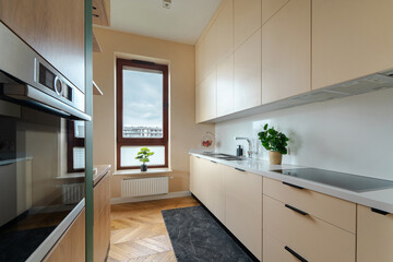 Modern apartment kitchen: sleek cabinets, light worktops, integrated appliances. Bright, functional cooking space with parquet flooring and a window for natural light. Great for everyday home life.