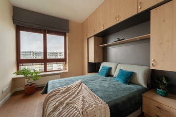Bedroom with bed in alcove of built-in light wood cabinets. Modern room has ample storage, large...