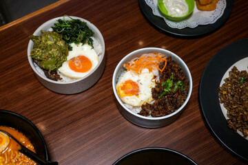 A bowl of rice with side dishes, likely dhal, green vegetables, and a boiled egg, arranged on a wooden table, creating a simple yet appetizing meal