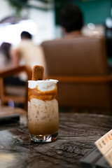 a layered iced coffee drink, likely a spiced cookie latte, served in a tall glass. It features layers of coffee, milk, and whipped topping, garnished with a spiced cookie.