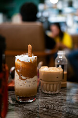a layered iced coffee drink, likely a spiced cookie latte, served in a tall glass. It features layers of coffee, milk, and whipped topping, garnished with a spiced cookie.