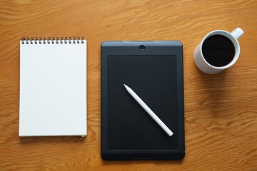 Tablet with stylus notepad and coffee cup on a wooden desk