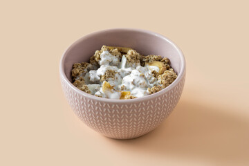 Yogurt with granola , high-resolution . Side view of a ceramic bowl with granola , banana and yoghurt on the light orange background . Muesli with fruit close-up . 