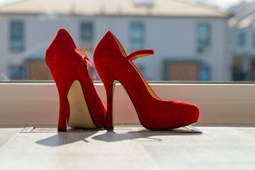 Red ladies pumps on the floor in front of a window