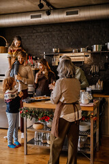 A White woman, two adult White parents, a school-aged boy, and a girl gather in a festive kitchen, eating cookies and celebrating Christmas around a decorated wooden table.