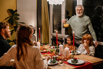 A multinational group of people of different ages enjoying Christmas dinner together, sitting at a...