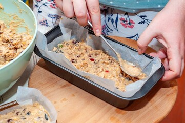 A person carefully spreads batter into a loaf pan, preparing a homemade fruitcake for baking.