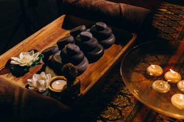 Flat lay of Thai spa essentials including stones, oils, lotus flowers, and towels arranged for a massage setting.