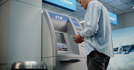 Cash Machine in Crowded Airport Terminal: Man Pressing Buttons on ATM Keypad, Entering PIN Code, Withdrawing Cash, Taking Money. Automated Teller Machine, Banking Services, Transactions. Medium Shot.