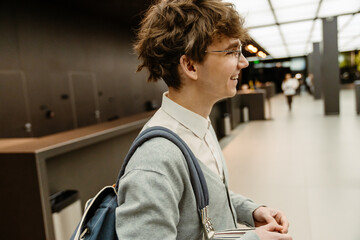A young White male office worker smiles while standing in a modern lobby of a business center. The concept of anticipation of a new workday and new beginnings.