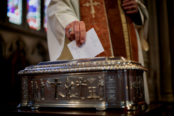 Priest putting donation in a silver box at a church ceremony symbolizing charity or giving.