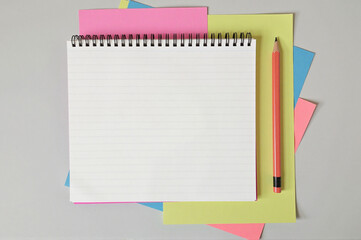 Notepad with a pencil resting on top of it, surrounded by a variety of colorful papers.