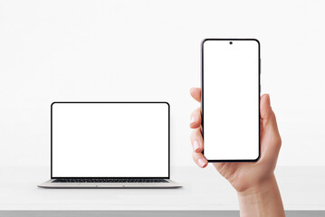 Plakat Smartphone in hand with blank screen and laptop in background on desk, both ready for UI or branding mockup
