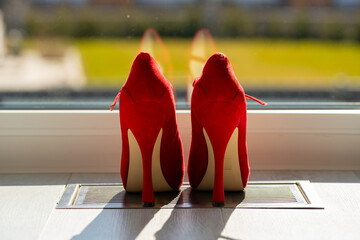Red ladies pumps on the floor in front of a window
