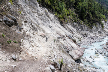 Trekker descending a narrow rocky trail between Bimtang and Tilche on the Manaslu Circuit in Nepal. Rugged slope above a glacier-fed river in the remote Himalayas