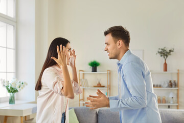 Young angry couple man and woman standing at home and arguing in quarrel. Unhappy husband and wife...