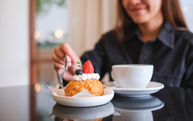 Closeup image of a woman eating a strawberry choux cream and coffee in cafe