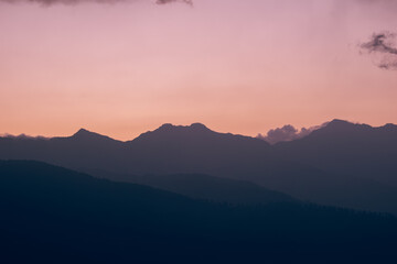 A serene mountain range silhouetted against a soft pink and orange sky during a peaceful sunset.