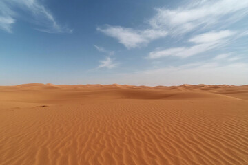 Vast desert landscape showcasing endless sand dunes under a bright blue sky with soft clouds at midday