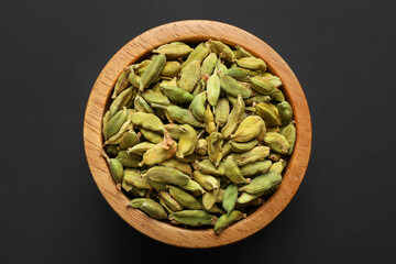 Dry cardamon seeds in bowl on dark table, top view