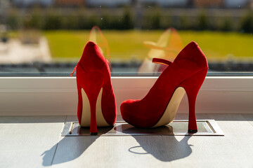 Red ladies pumps on the floor in front of a window