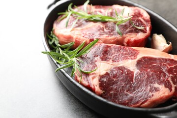 Pieces of raw beef meat and spices in baking dish on gray table, closeup
