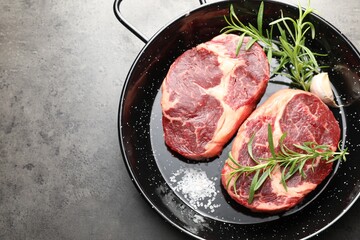 Pieces of raw beef meat and spices in baking dish on gray textured table, top view. Space for text
