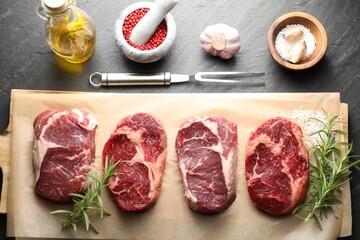 Pieces of raw beef meat, spices and carving fork on black table, flat lay
