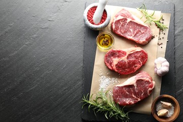 Pieces of raw beef meat and spices on black table, flat lay. Space for text