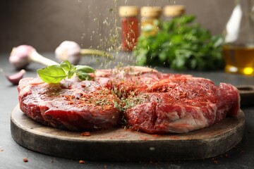 Sprinkling spices onto raw steaks on grey table, closeup