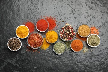 Different aromatic spices in bowls on dark table, flat lay