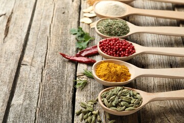 Different aromatic spices in spoons on wooden table, closeup. Space for text
