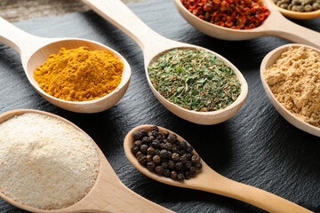 Different aromatic spices in spoons on black table, closeup
