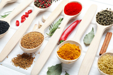 Different aromatic spices in spoons on white wooden table, closeup