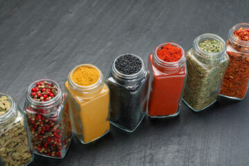 Different aromatic spices in jars on black table, closeup